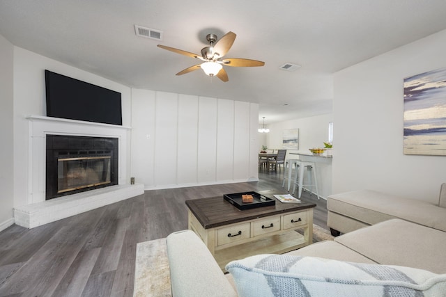 living area with ceiling fan with notable chandelier, visible vents, wood finished floors, and a glass covered fireplace