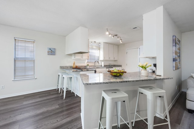 kitchen featuring baseboards, visible vents, dark wood-type flooring, a peninsula, and white cabinetry