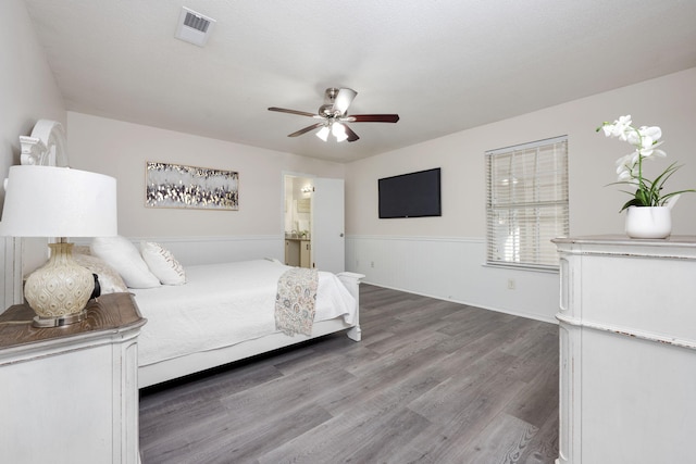 bedroom featuring visible vents, connected bathroom, wainscoting, ceiling fan, and wood finished floors