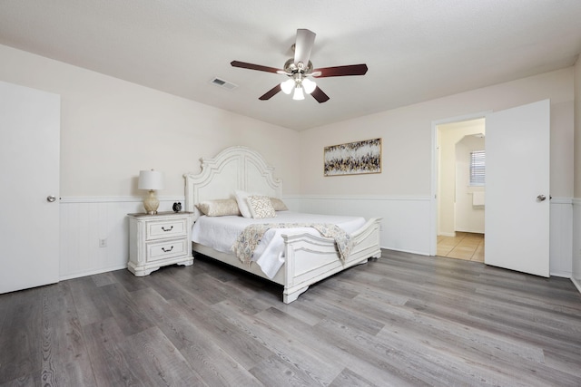 unfurnished bedroom with ensuite bathroom, wainscoting, wood finished floors, and visible vents