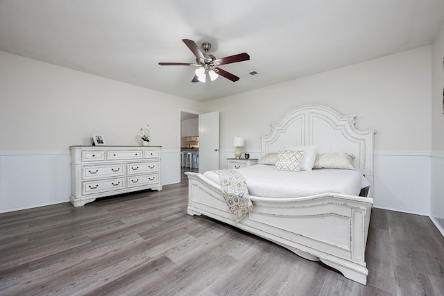 bedroom featuring wainscoting, wood finished floors, visible vents, and a ceiling fan