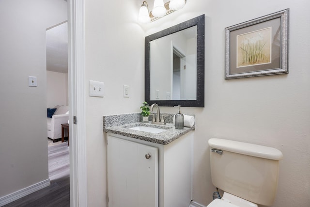 half bathroom with toilet, wood finished floors, vanity, and baseboards