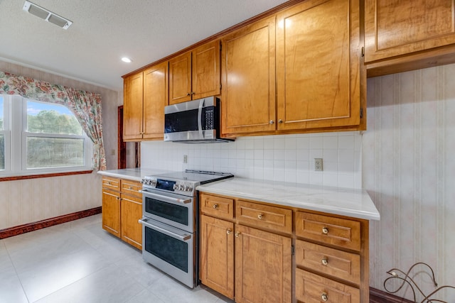 kitchen featuring tasteful backsplash, appliances with stainless steel finishes, light stone counters, and a textured ceiling