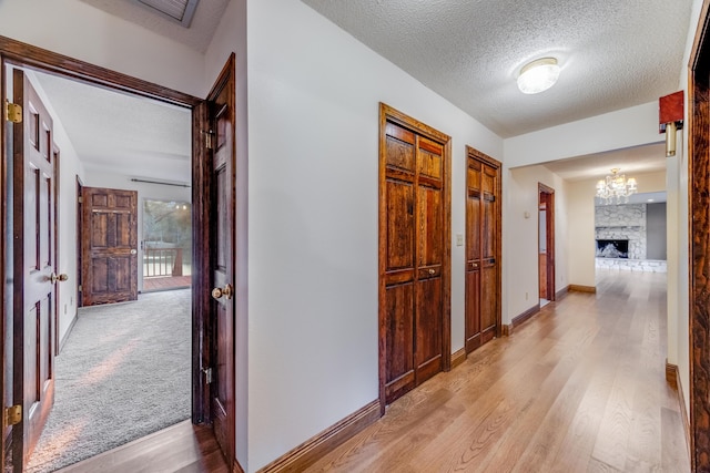 hallway with an inviting chandelier, a textured ceiling, and light hardwood / wood-style floors