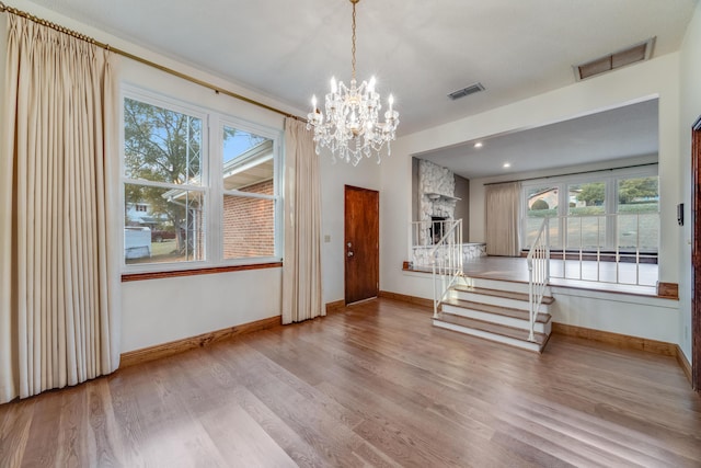 unfurnished dining area featuring a healthy amount of sunlight, light wood-type flooring, a fireplace, and an inviting chandelier