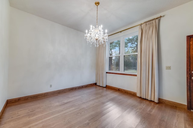 empty room featuring a notable chandelier and light wood-type flooring