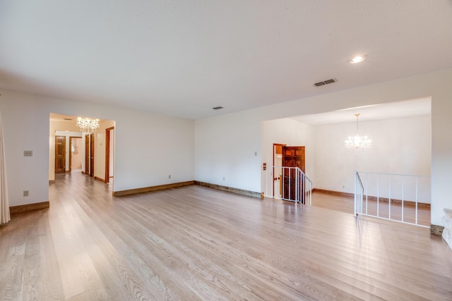 unfurnished living room with an inviting chandelier and light hardwood / wood-style floors