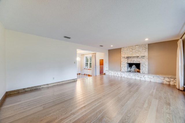 unfurnished living room featuring a stone fireplace, a textured ceiling, and light hardwood / wood-style flooring