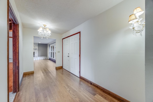 hall with light wood-type flooring, an inviting chandelier, and a textured ceiling