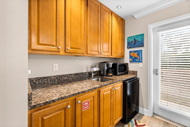 kitchen with ornamental molding, sink, light wood-type flooring, and dark stone countertops