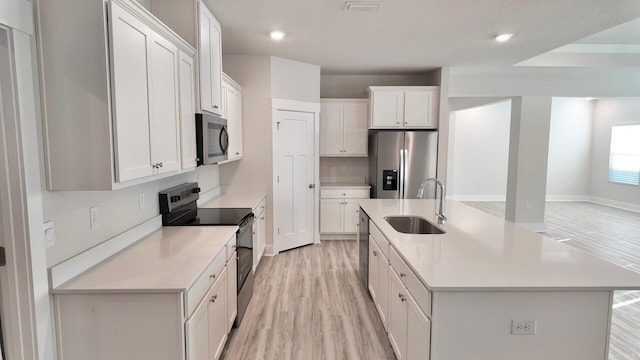 kitchen with a kitchen island with sink, a sink, stainless steel appliances, light wood-style floors, and white cabinets