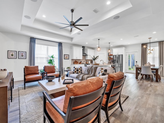 living room featuring ceiling fan with notable chandelier, a raised ceiling, and light hardwood / wood-style floors