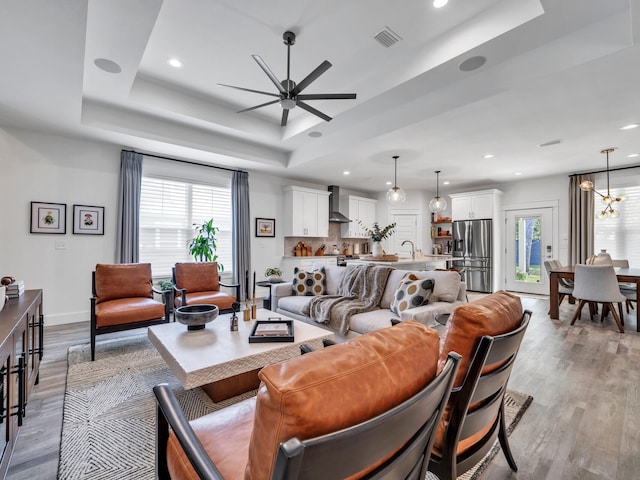 living room featuring sink, ceiling fan with notable chandelier, light hardwood / wood-style floors, and a raised ceiling