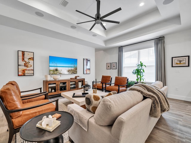 living room with ceiling fan, a raised ceiling, and light hardwood / wood-style floors