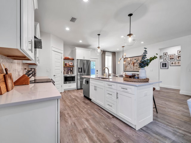 kitchen with white cabinetry, hanging light fixtures, sink, and a center island with sink