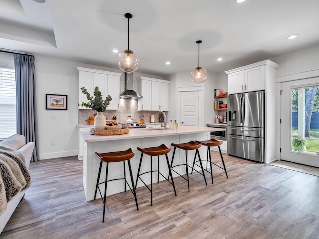 kitchen featuring pendant lighting, white cabinetry, appliances with stainless steel finishes, and wall chimney range hood