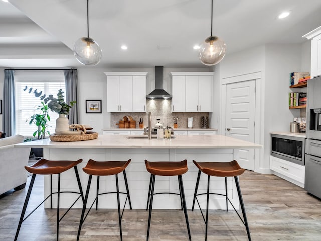 kitchen featuring built in microwave, wall chimney range hood, decorative light fixtures, and a kitchen island with sink