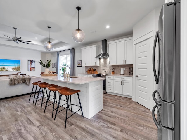 kitchen with stainless steel appliances, white cabinetry, a kitchen island with sink, and wall chimney range hood