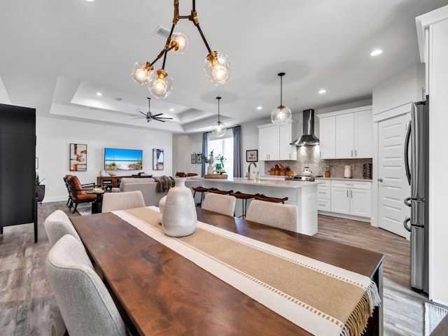 dining space featuring sink, a raised ceiling, ceiling fan, and light wood-type flooring