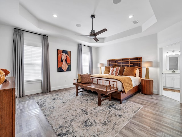 bedroom with sink, connected bathroom, a tray ceiling, and light hardwood / wood-style floors