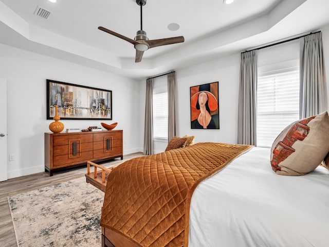 bedroom with light hardwood / wood-style flooring, a raised ceiling, and ceiling fan