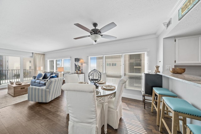 dining area featuring a textured ceiling, dark wood-type flooring, crown molding, and ceiling fan