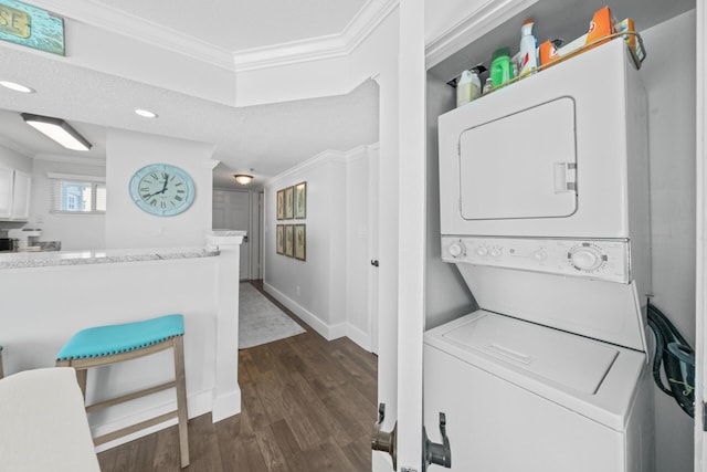 washroom with dark hardwood / wood-style flooring, stacked washer / dryer, and crown molding