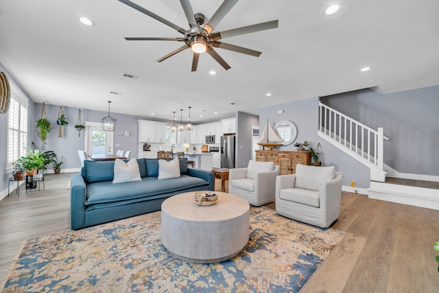 living room with ceiling fan with notable chandelier and light hardwood / wood-style flooring