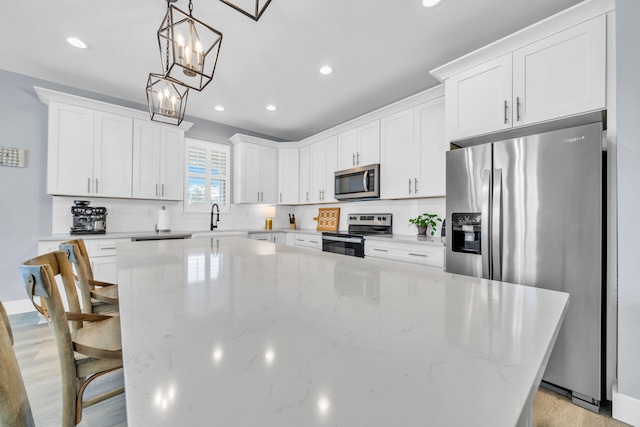 kitchen featuring decorative light fixtures, white cabinetry, appliances with stainless steel finishes, and a center island