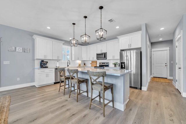 kitchen with hanging light fixtures, white cabinets, a kitchen bar, a kitchen island, and stainless steel appliances