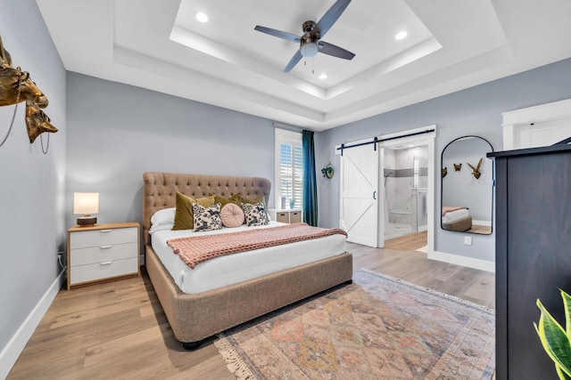 bedroom with ceiling fan, a tray ceiling, ensuite bath, and a barn door