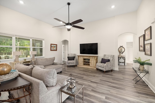 living room featuring hardwood / wood-style flooring, ceiling fan, and a towering ceiling