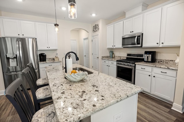 kitchen featuring appliances with stainless steel finishes, an island with sink, white cabinetry, and hanging light fixtures