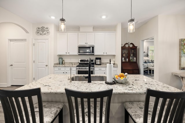 kitchen featuring a center island with sink, white cabinetry, stainless steel appliances, and decorative light fixtures