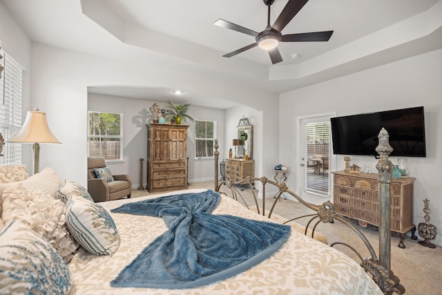 carpeted bedroom featuring ceiling fan, a tray ceiling, and access to exterior