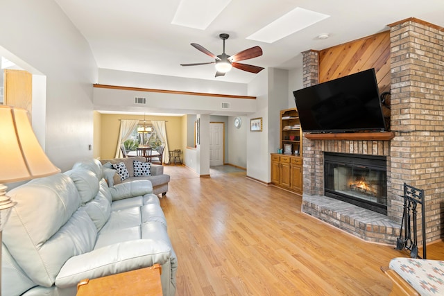 living room with ceiling fan, a brick fireplace, light hardwood / wood-style floors, and a skylight