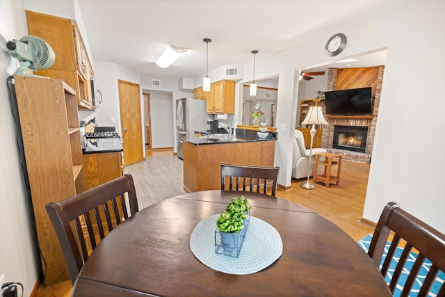 dining area featuring ceiling fan, a brick fireplace, sink, and light hardwood / wood-style floors