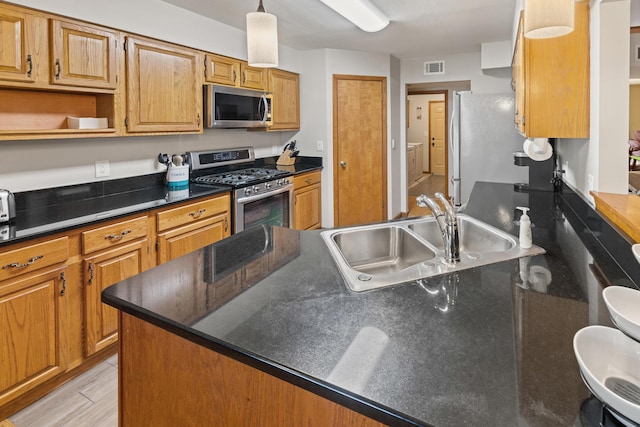 kitchen featuring sink, appliances with stainless steel finishes, hanging light fixtures, washer / dryer, and light wood-type flooring