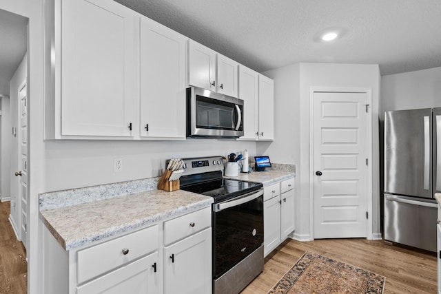 kitchen with a textured ceiling, appliances with stainless steel finishes, white cabinets, and light wood-type flooring