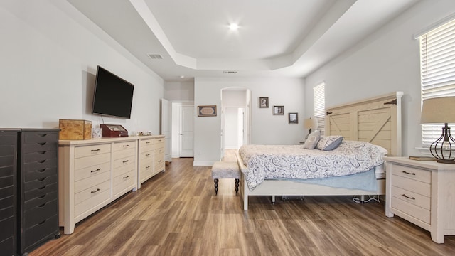 bedroom featuring arched walkways, wood finished floors, a raised ceiling, and visible vents