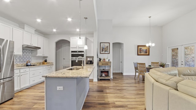 kitchen with stainless steel appliances, arched walkways, a sink, and under cabinet range hood