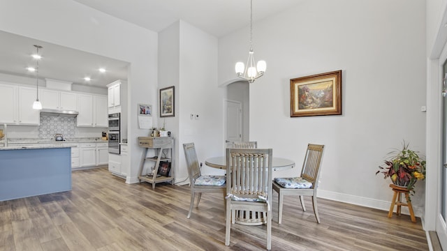 dining room with arched walkways, a high ceiling, light wood-style floors, a chandelier, and baseboards