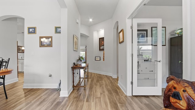 hallway featuring arched walkways, light wood-style flooring, and baseboards