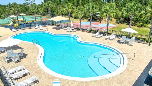 pool featuring fence, playground community, and a patio