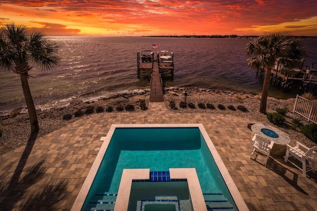 pool at dusk with an outdoor fire pit, a patio area, a water view, and a pool with connected hot tub