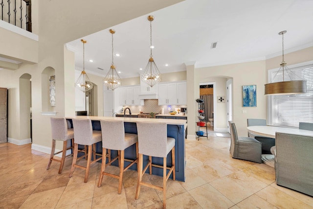 kitchen featuring a large island with sink, decorative light fixtures, white cabinetry, a kitchen breakfast bar, and backsplash