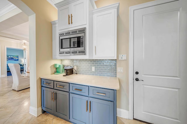 kitchen with white cabinets, backsplash, stainless steel microwave, and ornamental molding