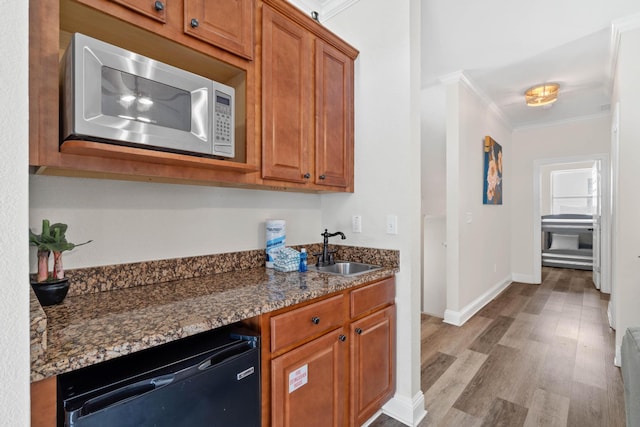 kitchen with dark stone countertops, sink, black dishwasher, light wood-type flooring, and ornamental molding