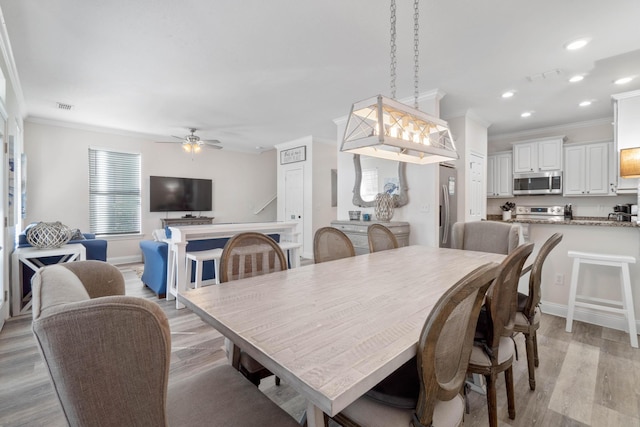 dining space with ceiling fan, ornamental molding, and light wood-type flooring