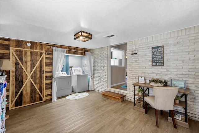 interior space featuring brick wall, wood-type flooring, independent washer and dryer, and a barn door